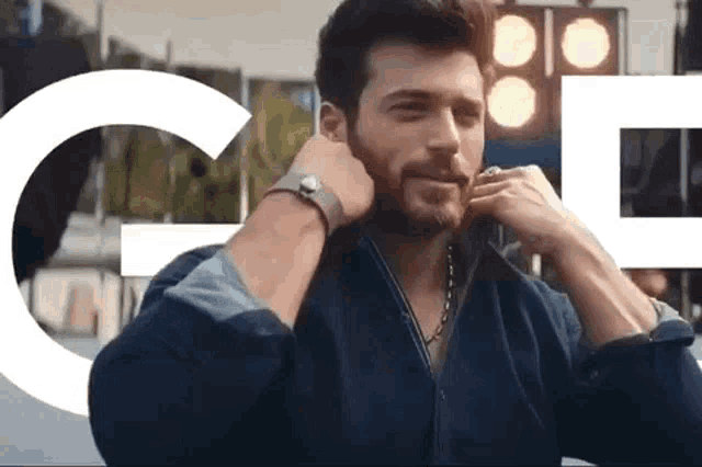 a man with a beard is wearing a watch and a necklace while talking on a cell phone .