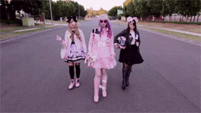 three girls are walking down a street with one wearing a pink dress and a black jacket