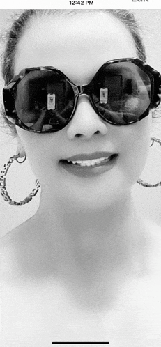 a woman wearing sunglasses and hoop earrings is smiling in a black and white photo
