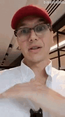 a man wearing glasses , a red hat and a white shirt is making a face .