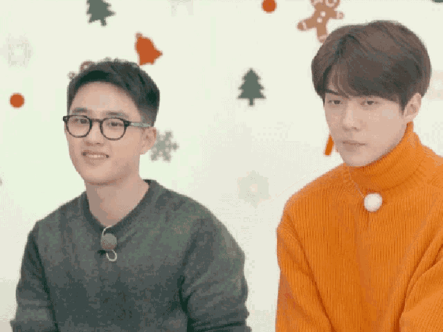 a man wearing glasses and an orange sweater is standing next to another man