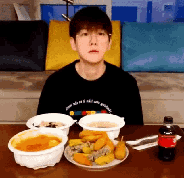 a young man is sitting at a table with a plate of food and a bottle of coca cola