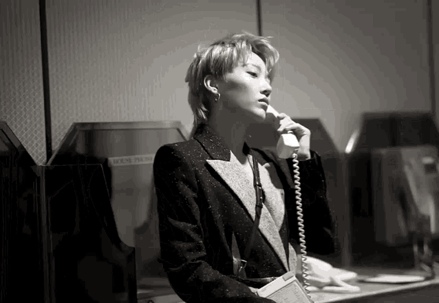 a black and white photo of a woman talking on a telephone in front of a box that says house telephone