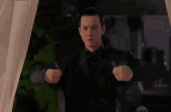 a man in a suit and bow tie is standing in front of a curtain .