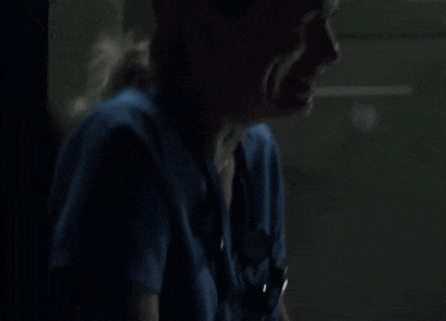 a woman in a blue shirt is crying in the dark while sitting in front of a window .