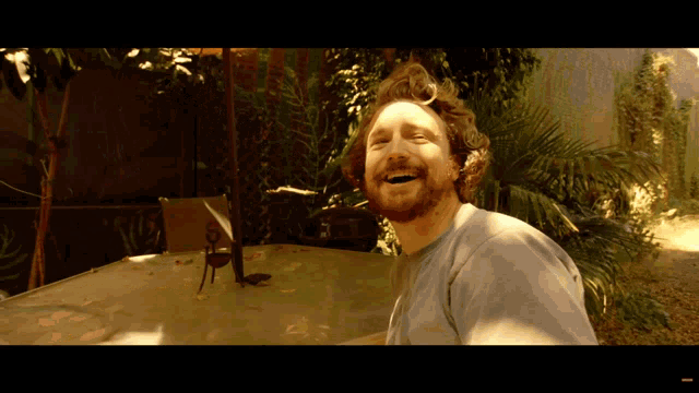 a man with a beard is smiling while sitting at a table outside