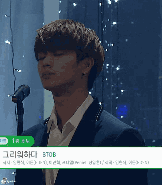 a man in a suit singing into a microphone with the name btob on the bottom of the screen
