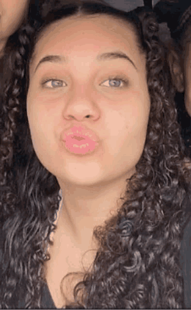 a woman with curly hair is making a funny face with her lips .