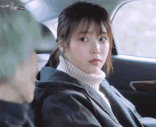 a woman wearing a sweater and a jacket is sitting in a car with a man