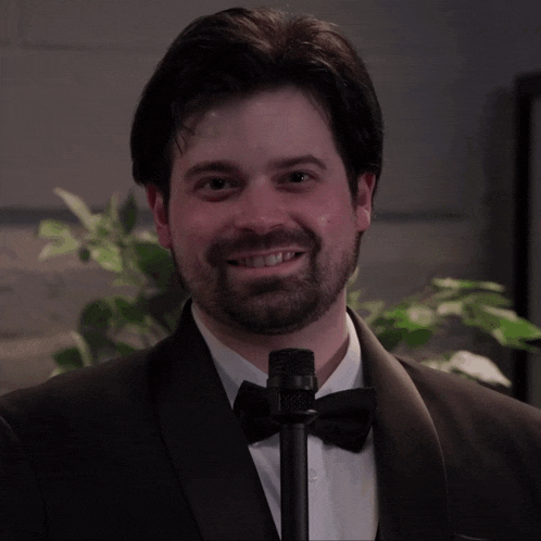 a man in a tuxedo and bow tie is holding a microphone and smiling