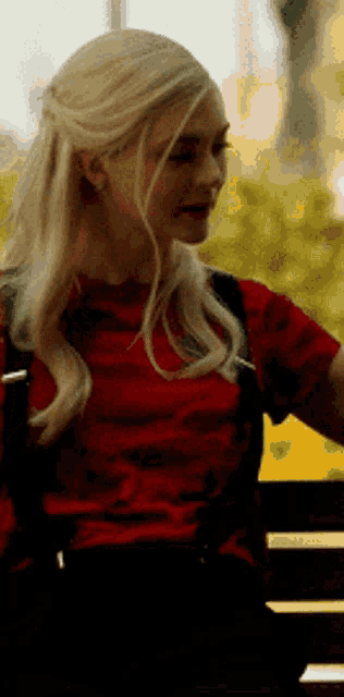 a woman with blonde hair is wearing a red shirt and a backpack .
