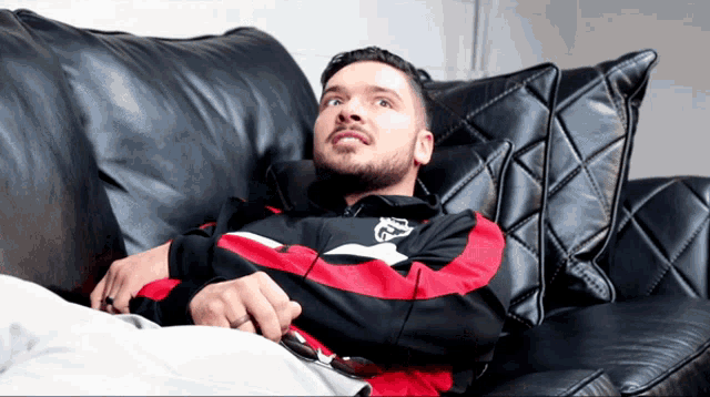 a man is laying on a black leather couch with a red and black jacket