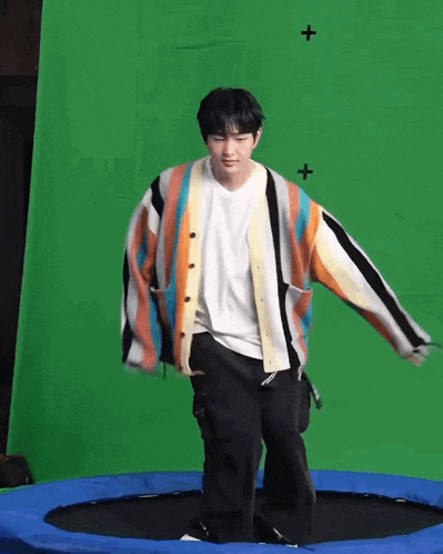 a young man is standing on a trampoline with a green screen behind him .