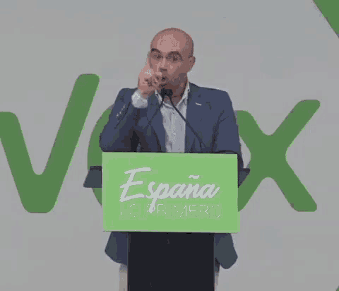 a man stands at a podium with a green sign that says espana lo primero