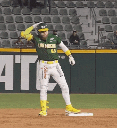 a baseball player wearing a green los mochi jersey stands on the base
