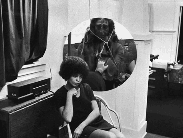 a woman sits in a chair in front of a mirror with a picture of a man behind her
