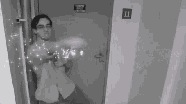 a black and white photo of a man standing in front of a door with the number 11 on it .