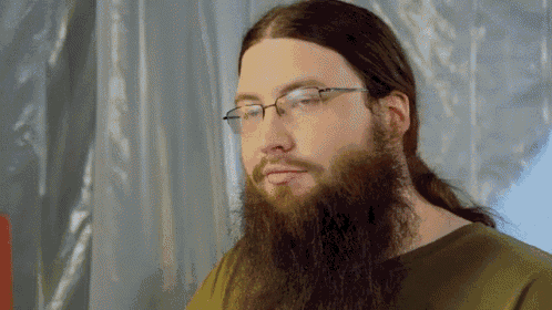 a man with a long beard and glasses looks at the camera
