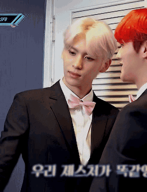 a man in a suit with a pink bow tie is standing next to another man with red hair