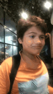a young boy wearing an orange shirt and a backpack is standing in a room .