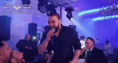 a man with a beard is singing into a microphone in front of a crowd of people .