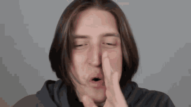 a man with long hair is blowing a kiss with his finger to his face .