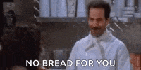 a man in a chef 's uniform is talking to a woman in a kitchen and saying `` no bread for you '' .