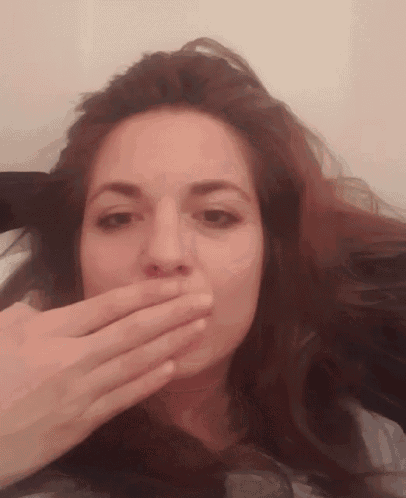 a woman covering her mouth with her hand while looking at the camera