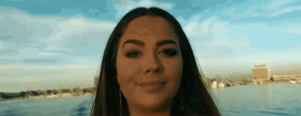 a close up of a woman 's face while standing in front of a body of water .
