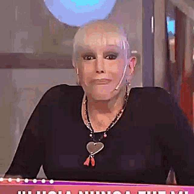 a woman wearing a black shirt and a heart necklace is sitting at a table with a microphone .