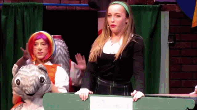 a girl with a green headband is standing next to a stuffed animal
