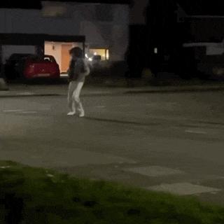 a person is walking down a street at night in front of a house .