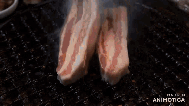 two pieces of meat are being cooked on a grill with smoke coming out of it .
