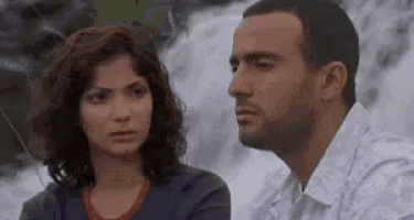 a man and a woman are sitting in front of a waterfall .