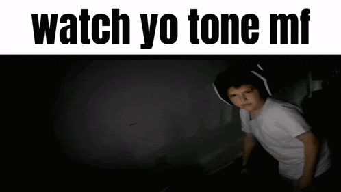 a young boy wearing headphones is standing in a dark room with the words `` watch yo tone mf '' above him .