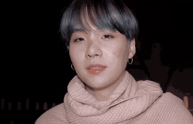 a young man with braces on his teeth is wearing a pink sweater and earrings .