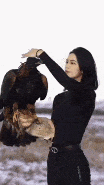 a woman in a black shirt is holding a large bird on her arm .