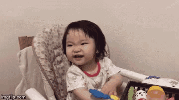 a baby girl is sitting in a high chair playing with a toy .