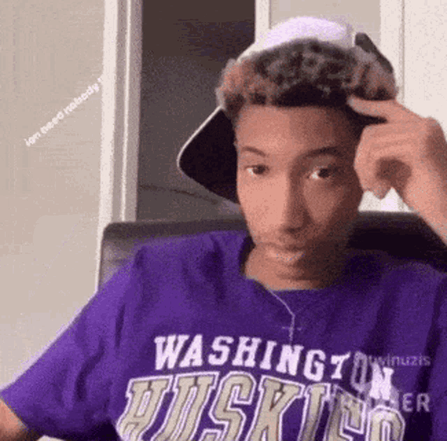 a young man wearing a washington huskies t-shirt and a hat is sitting in a chair .