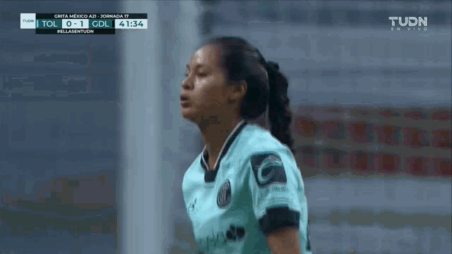 a woman in a soccer uniform stands in front of a tv screen that says tudn on it