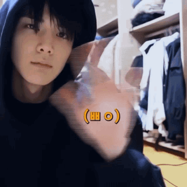 a young man wearing a hoodie is waving his hand in front of a closet full of clothes ..