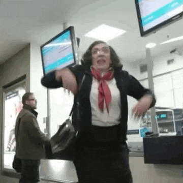 a woman in a red scarf is dancing in a room with a man in a brown coat standing behind her .