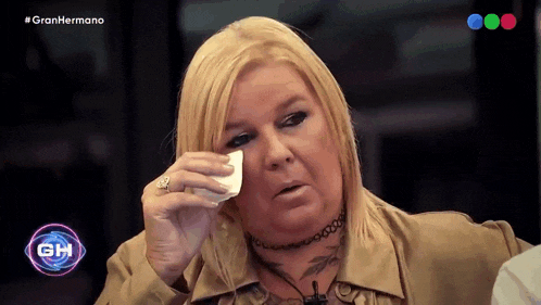 a woman wipes her face with a tissue in front of a sign that says gran hermano