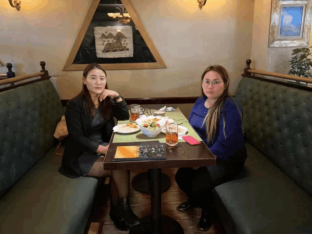 two women sit at a table with plates of food and a menu that says ' dinner ' on it