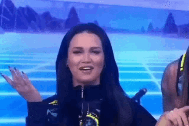 a woman with long black hair is standing in front of a microphone and making a funny face .