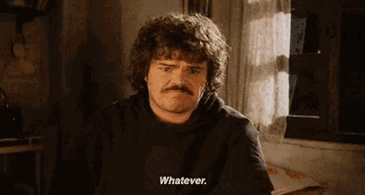 a man with curly hair and a mustache is sitting at a table and saying whatever .