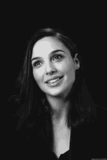a black and white photo of a woman smiling in a black background .