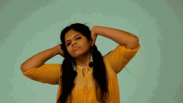 a woman in a yellow shirt is making a funny face with her hands in her hair