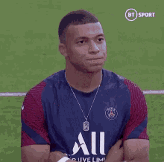 a soccer player is sitting on the field with his arms crossed and looking at the camera .