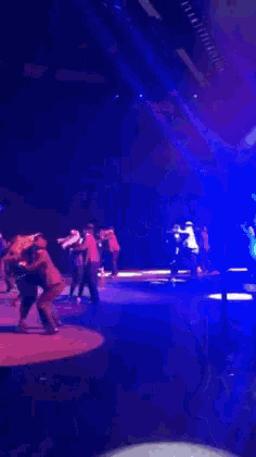 a group of people dancing on a stage with blue lights behind them